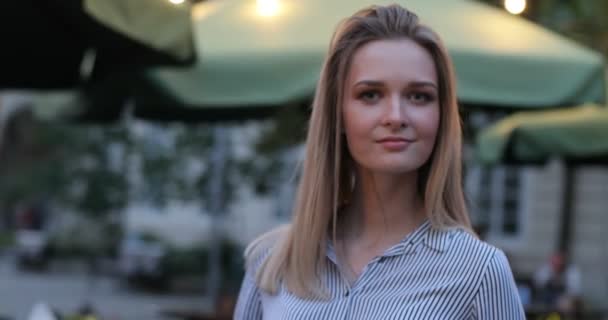 Round view of a pretty blonde lady looking at the camera and smiling. Close-up evening view. — Stock Video