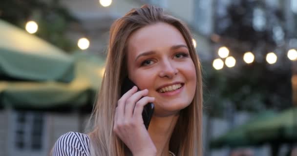 Joven hermosa hembra está respondiendo a su teléfono y sonriendo en la calle por la noche. Rubia con ojos azules. Retrato de primer plano . — Vídeos de Stock