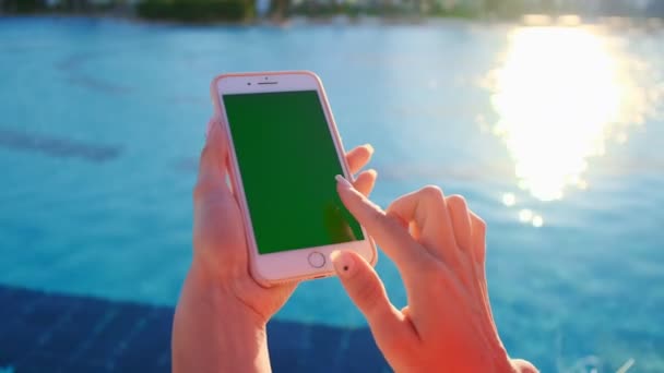 Close up of girl using mobile phone green screen while relaxing near the swimming pool. Hands holding smartphone chrome key, fingers tapping modern display smart phone, scrolling functions messaging — Stock Video