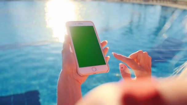 Primer plano de la chica usando la pantalla verde del teléfono móvil mientras se relaja cerca de la piscina. Las manos que sostienen la tecla de cromo smartphone, dedos tocando el teléfono inteligente pantalla moderna, funciones de desplazamiento de mensajería . — Vídeos de Stock