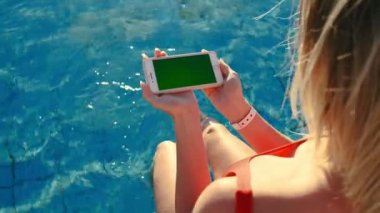 Yüzme Havuzu dinlenirken yatay hareket eden telefon yeşil ekran kullanan kız. Eller Smartphone krom tuşunu basılı tutarak, modern dokunarak parmak akıllı telefon, mesajlaşma işlevlerini kaydırma görüntülemek..
