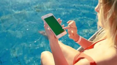 Yüzme Havuzu dinlenirken dikey cep telefonu yeşil ekran kullanan kız. Eller Smartphone krom tuşunu basılı tutarak, modern dokunarak parmak akıllı telefon, mesajlaşma işlevlerini kaydırma görüntülemek..