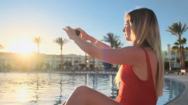 Genç kadın telefon ile sunset yakınında lüks villa yüzme havuzunda yorgunluk çekiyor. Sarışın kız Foto, yapma video kamera için smartphone ekran holding eller ile güneşin yakın çekim