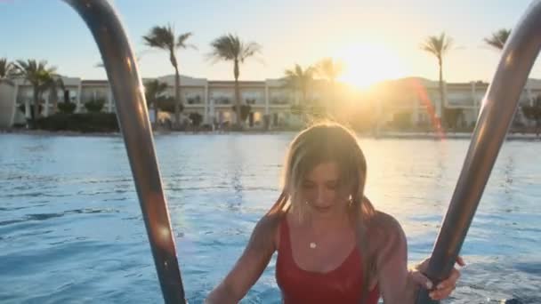 Nahaufnahme Porträt einer attraktiven jungen Frau in feuchtrotem Badeanzug aus dem blauen Swimmingpool an einem heißen, sonnigen Tag. Bikini-Girl hat Spaß im Sommerurlaub, blickt in die Kamera — Stockvideo