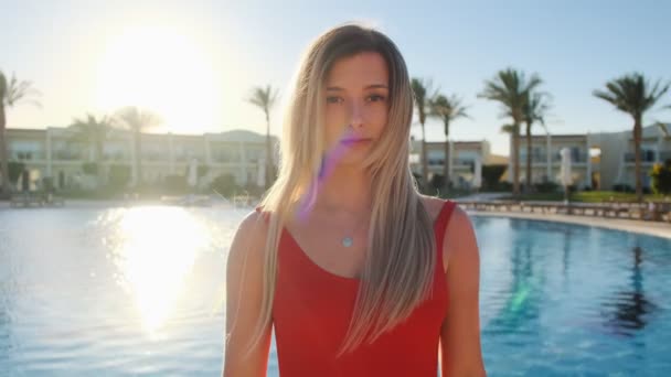 Portret van lachende jong meisje, camera kijken. Mooie vrouw in rode zwembroek in de buurt van het blauwe zwembad op warme zonnige dag. Meisje met goede tijd, zomervakantie bij luxe hotel achtergrond. — Stockvideo