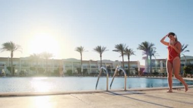 Güzel kadın kırmızı mayo ve kulaklık, Yüzme Havuzu ile yürüyüş smartphone cep telefonu ile müzik dinleme. İyi vakit geçiriyor, lüks Villa Yüzme Havuz kenarında rahatlatıcı bikini kız portresi.