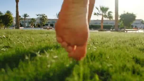 Close up of young girl legs running barefoot on the green grass. Slow motion shot of bare feet of young girl walking on fresh grass from hotel room to swimming pool. — Stock Video