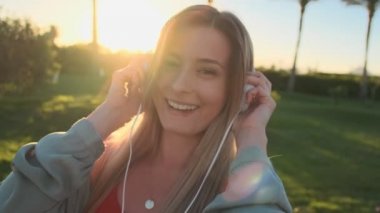 Smartphone cep telefonu ile app kullanarak müzik dinleme genç çekici kadın kırmızı mayo beyaz kulaklık giyen neşeli gülümseyen boby portresi kapatın. Güneş ve palmas arka plan.