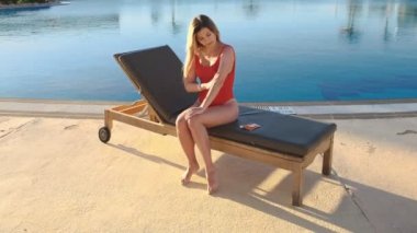 Cildi korumak ve güneşten gelen yaşlanma önlemek için çekici kız kırmızı mayo tabaklanmış deri üzerinde güneş krem uygulamak. Egzotik resort havuz yan yakınındaki güneş banyosu.
