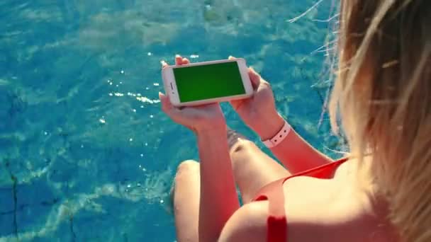 Chica usando la pantalla verde del teléfono móvil horizontal mientras se relaja cerca de la piscina. Las manos que sostienen la tecla de cromo smartphone, dedos tocando el teléfono inteligente pantalla moderna, funciones de desplazamiento de mensajería . — Vídeos de Stock
