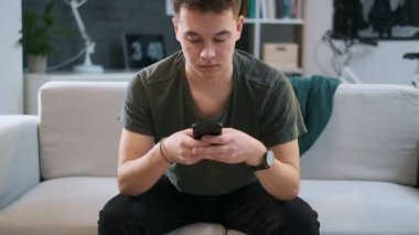 Yakışıklı genç akıllı telefonunda yazıyor ve kanepede oturuyor.