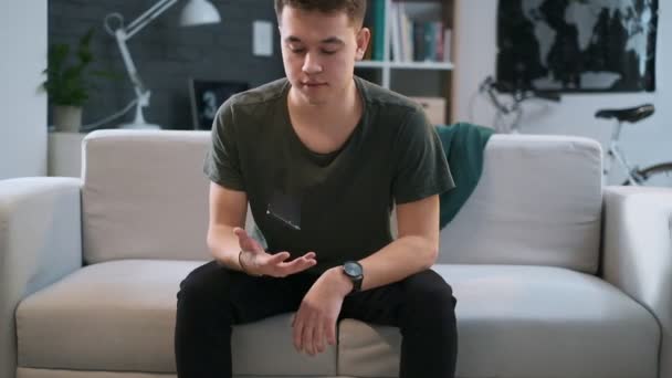 Un garçon lance un téléphone portable dans sa main alors qu'il est assis sur un canapé dans sa chambre . — Video