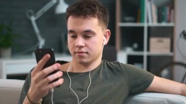 Genç çocuk kulaklıklarıyla müziğin tadını çıkarıyor ve telefonundaki bir uygulamayla birine mesaj atıyor.