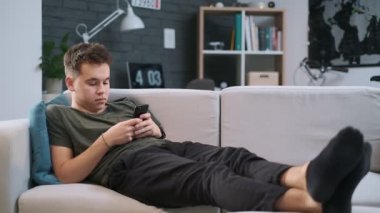 Bir genç elinde telefon ile bir kanepede yatıyor ve web sörf