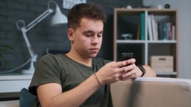 Evde bir kanepede otururken akıllı telefonunda yazan genç bir çocuğun yakın çekim portresi