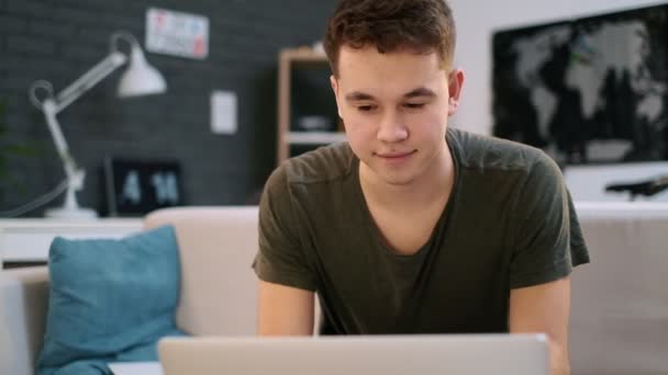 Ein jugendlicher kaukasischer Junge arbeitet glücklich am Laptop in seinem Zimmer und nickt mit dem Kopf — Stockvideo