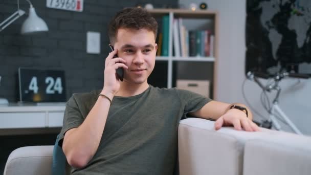 Podrobný pohled na hezkého teenagera, jak mluví na telefonu a přitom odpočívá na pohovce ve svém pokoji — Stock video