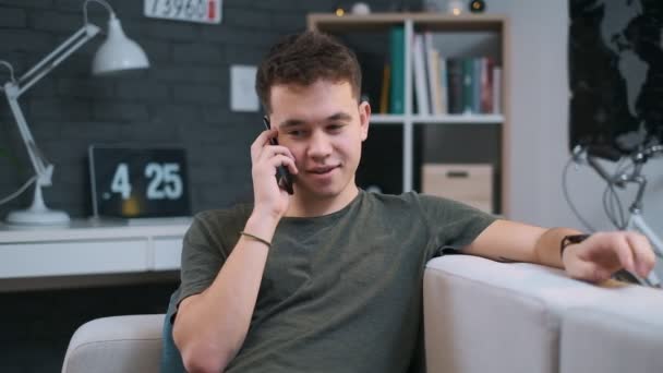 A cute teenager is talking on the phone and fidgeting his hand, close-up front view indoors — Stock Video