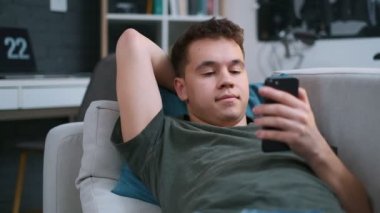 Bir genç kanepede yatıyor ve evde akıllı telefon kullanarak, yakın çekim, yüz odaklanmak