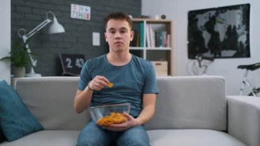 Bir kanepede oturan ve evde cips yemek sıkılmış bir gencin ön görünümü