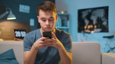 Genç bir çocuk arka planda açık masa lambası ile akşam evde akıllı telefonda web tarama