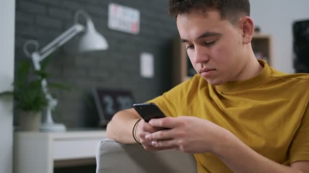 Close-up vídeo de um adolescente digitando algo em seu smartphone, quarto elegante em um fundo — Vídeo de Stock