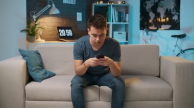 Yakışıklı bir genç çocuk onun akıllı telefon bir şey yazıyor ve sonra bitirdikten sonra kanepede geri dinlenir