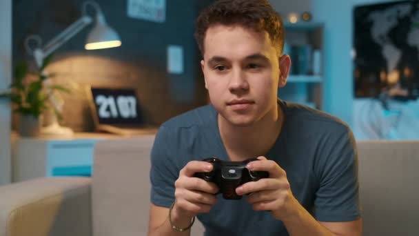 Adolescente jugando un videojuego con un controlador en el sofá, decepcionándose al final porque perdió — Vídeo de stock