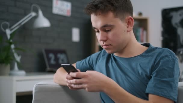 Крупный план мальчика-подростка, печатающего сообщение на мобильном телефоне в своей комнате — стоковое видео