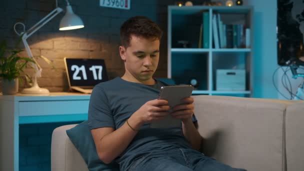 Передній вигляд молодого хлопчика, який грає на планшеті на дивані в кімнаті . — стокове відео