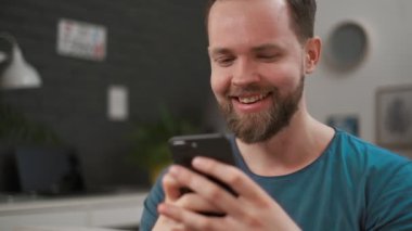 Yakışıklı bir adamın yakın portresi ni yazarak ve evde akıllı telefonuna mesaj. Erkek internettarama dijital mobil cihaz kullanarak, dinlenirken evde bağlı kalmak.