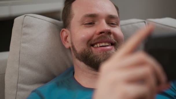 Retrato de close-up de um homem bonito digitando e mensagens de texto em seu smartphone em casa. Masculino usando dispositivo móvel digital navegando na internet, permanecendo conectado em casa enquanto relaxa . — Vídeo de Stock