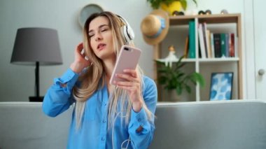 Kulaklık ile müzik dinleme rahat oturma odası arka planda Genç Sevimli çekici genç kız portre. Mavi bluz giyen kadın müzik zevk ve evde dans.