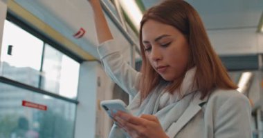 Sevimli kız portresi, toplu taşımacılığında cep telefonunda parmaklık, manifatura ve tarama tutar. Şehir, kentsel arka plan.