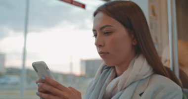 Akıllı telefon tarama internet ve arkadaşlarınızla sohbet kullanarak toplu taşıma çekici gülümseyen kız yakın yukarı portre. Tramvay üzerinde seyahat ederken sevimli kadın, el parmaklık tutar. Şehir, kentsel.