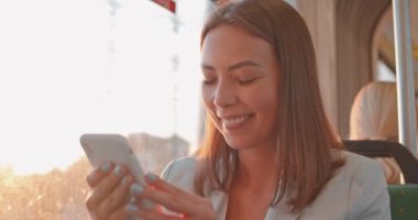 Akıllı telefon, sohbet ve arkadaşlarınızla manifatura kullanarak toplu taşıma çekici gülümseyen esmer kız yakın yukarı portre. Kentsel, şehir geçmişi. Gün ışığı