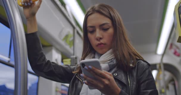 Retrato de mulher morena bonito detém o corrimão, mensagens de texto e navegação no telefone móvel no transporte público. Cidade luzes fundo . — Vídeo de Stock