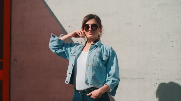 Retrato da jovem mulher branca bonita nos óculos de sol e roupa elegante posando como um modelo e sorrindo sob uma luz solar. Ao ar livre . — Vídeo de Stock