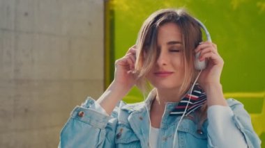 Sevimli neşeli genç Beyaz kadın kulaklık alarak yakın, müzik dinlemek ve mutlu şehir dışında sarı cam arka plan dans.