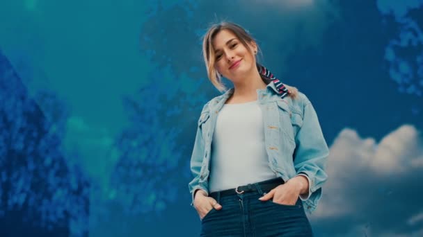Портрет, снятый снизу на кавказскую привлекательную стильную молодую девушку в синей джинсовой куртке, позирующую и улыбающуюся в камеру на голубом стекле задним узором с небом в ней снаружи . — стоковое видео
