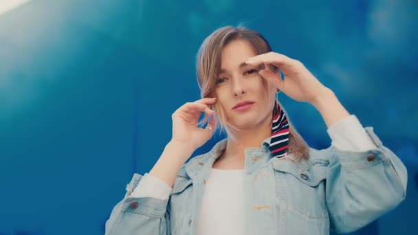 Portret van de aantrekkelijke en stijlvolle jonge Kaukasische vrouw staande op de blauwe glazen achtergrond en poseren voor de camera wih een glimlach. — Stockvideo