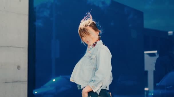 Posteriore della giovane donna caucasica elegante in piedi all'aperto sulla strada sullo sfondo di vetro blu, poi voltandosi verso la fotocamera e ridendo gioiosamente. Vista posteriore . — Video Stock