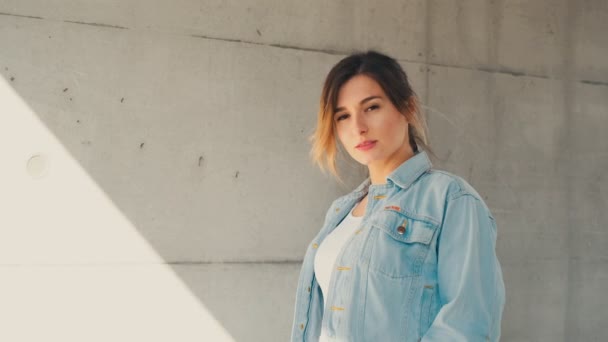 Retrato tiro da mulher branca jovem elegante e atraente na jaqueta jeans olhando para a câmera e sorrindo enquanto está de pé ao ar livre . — Vídeo de Stock