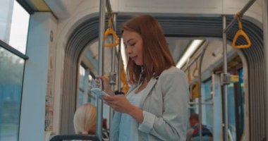 Kulaklık sevimli esmer kız Portresi toplu taşıma cep telefonu tarama tırabzan tutar. Akıllı telefonu kullanan kadın kulaklıkla müzik dinlemesohbeti yapıyor