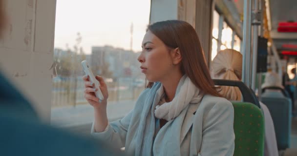 Retrato de linda chica seria mensajes de texto y navegación en el teléfono móvil en el transporte público. Triste mujer mirando por la ventana de un tren. Chica cansada y deprimida pensando en algo durante su viaje diario . — Vídeo de stock