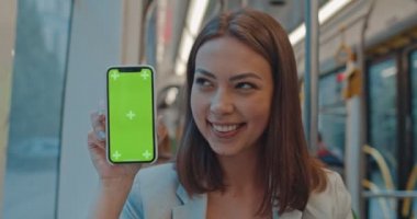 Toplu taşımada dikey yeşil ekranlı akıllı telefonu gösteren kız. Kroma tuşu ile cep telefonu tutan ve gidip sırasında jest kadar başparmak gösteren kadın.