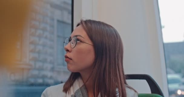 Portrait de jeune jolie fille souriante portant des lunettes regardant la caméra pendant le trajet dans les transports en commun. Ville, milieu urbain. Femme en attente d'un bus pour l'emmener à destination . — Video