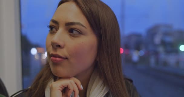 Retrato facial de una joven y atractiva chica sonriente mirando a la cámara durante el viaje en transporte público por la noche con luces de la ciudad. Tráfico de coches en segundo plano. Ciudad nocturna, fondo urbano . — Vídeo de stock