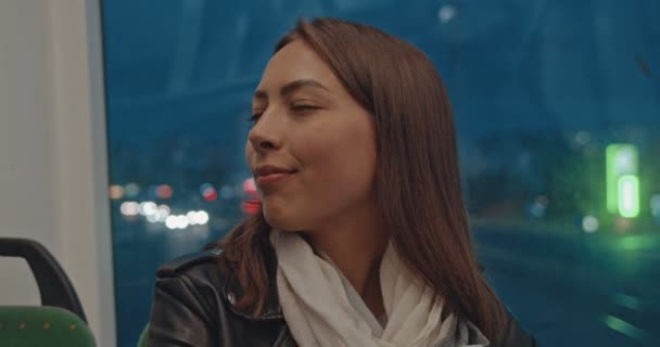 街の明かりの夜に公共交通機関に乗っている間にカメラを見て若い魅力的な笑顔の女の子の肖像画。バックグラウンドでの車のトラフィック。夜の都市、都市の背景. — ストック動画