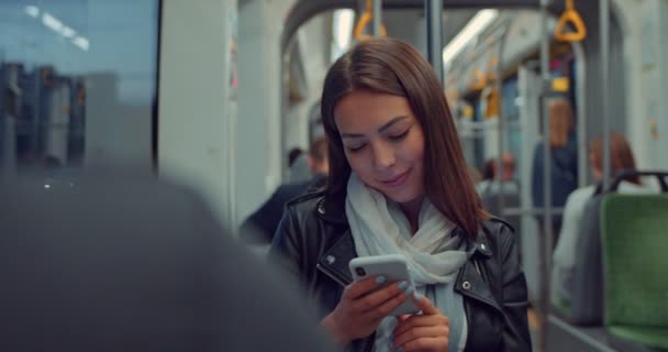 Retrato de chica atractiva joven usando smartphone durante el viaje en tranvía por la noche en la ciudad. Mujer en transporte público usando smartphone navegando por internet y charlando con amigos — Vídeo de stock